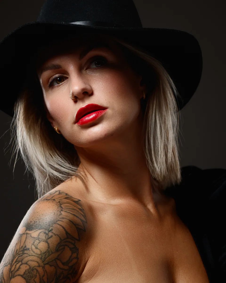 Woman in a black hat with red lipstick and a shoulder tattoo