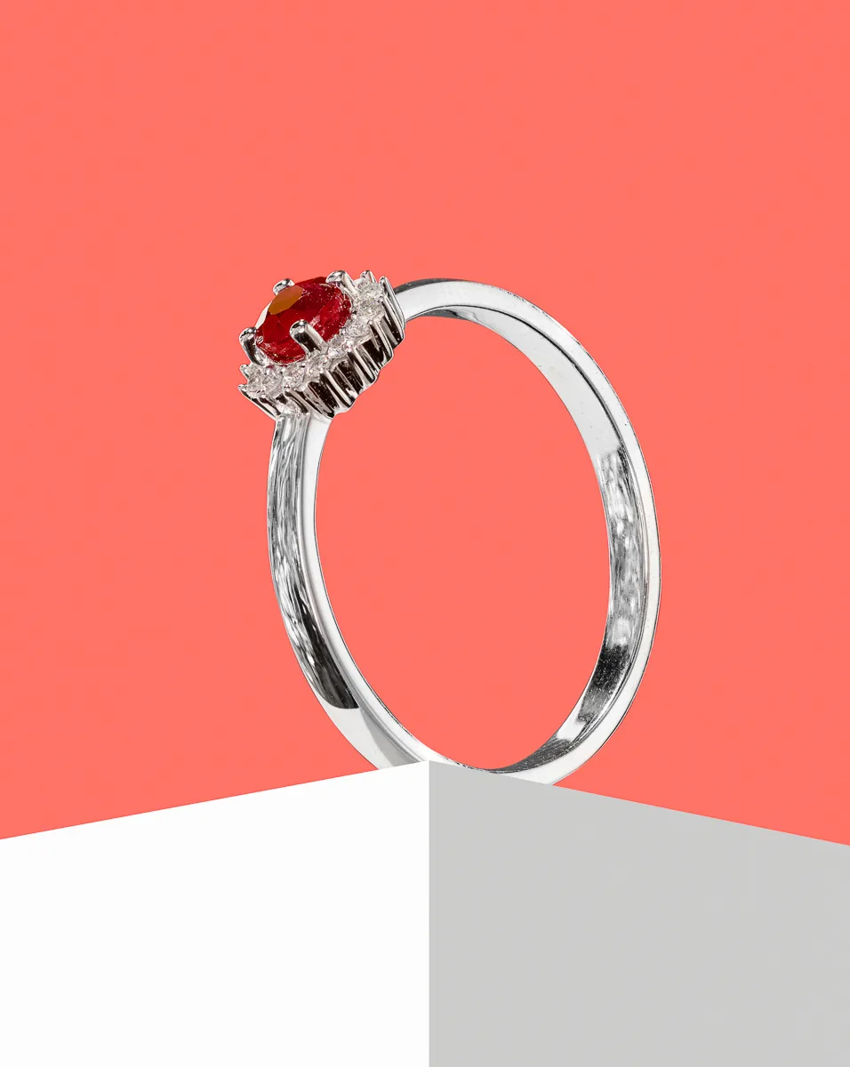 Silver ring with red gemstone on white block.
