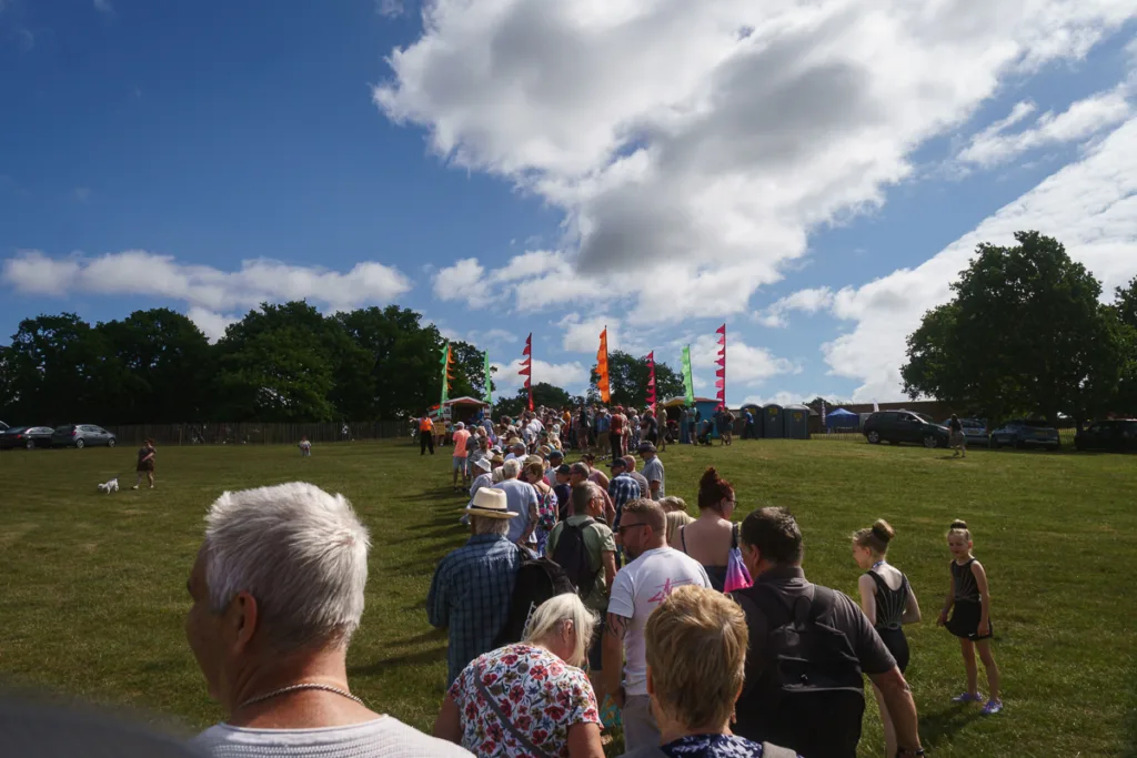 Crowd gathering on grassy field with colourful flags.