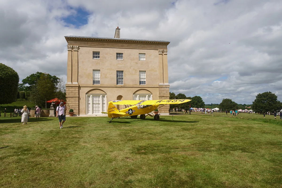 Yellow vintage plane by historic building on grass