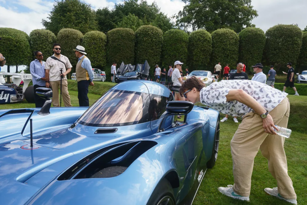 People admiring luxury blue sports car outdoors event.