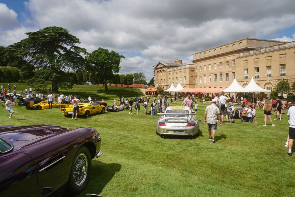 Classic car show on mansion lawn with visitors