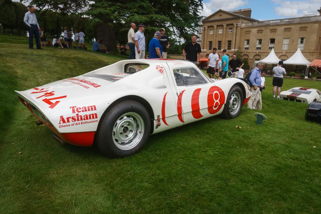 Vintage sports car displayed on lawn outside manor.