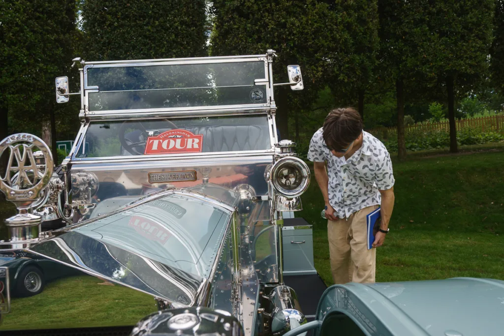 Person inspecting vintage car at outdoor event.