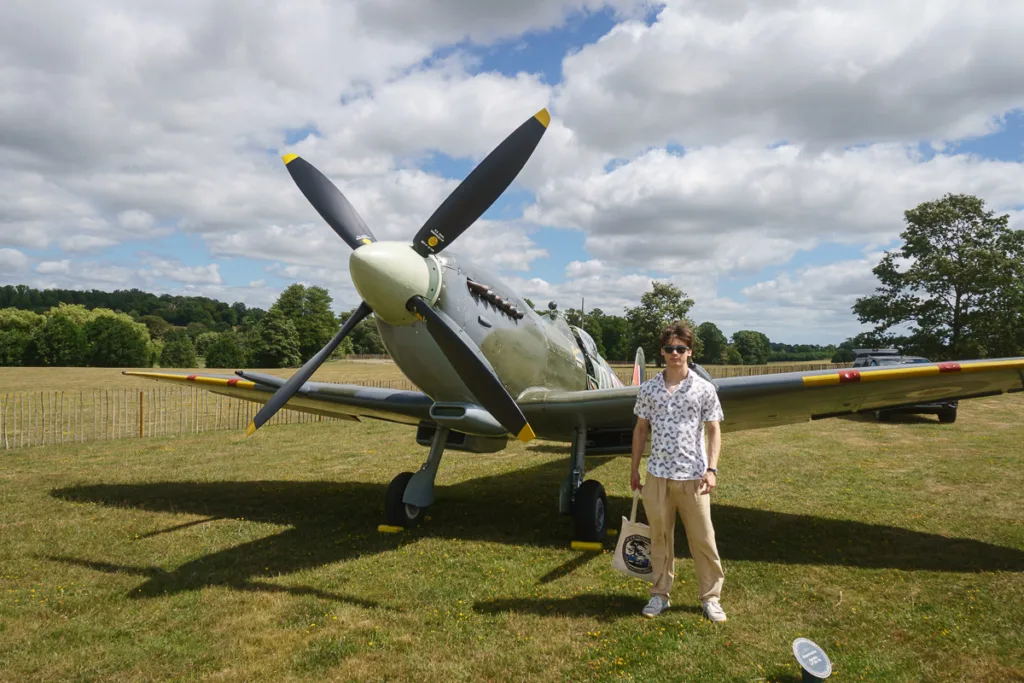 Person standing by vintage aircraft on grassy field.