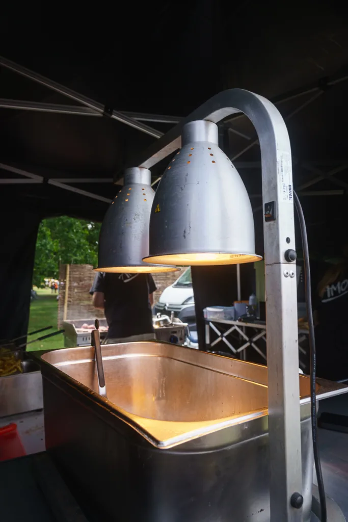 Stainless steel heat lamp over food tray at fair.