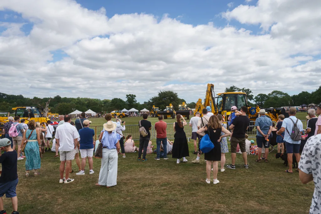 Crowd watching diggers at outdoor event.