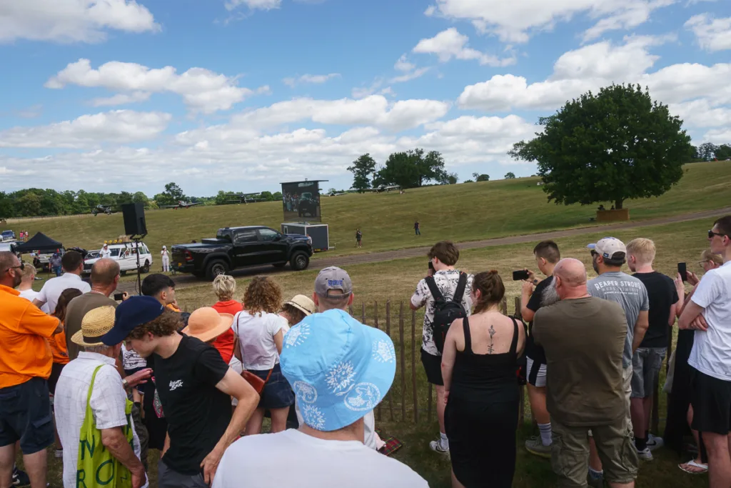 Crowd watching outdoor event with vehicles and planes.