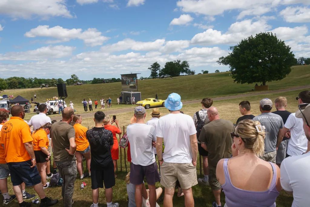 Crowd watching classic car display outdoors.