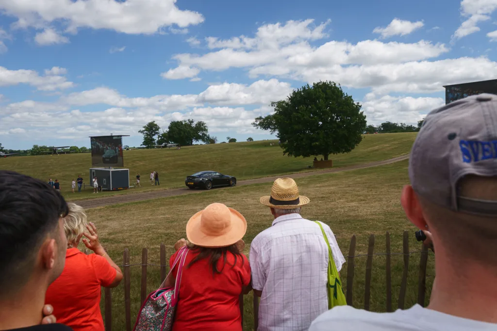 Crowd watching car at outdoor event.