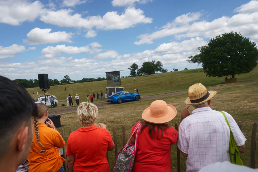 Spectators watching blue car at outdoor event.