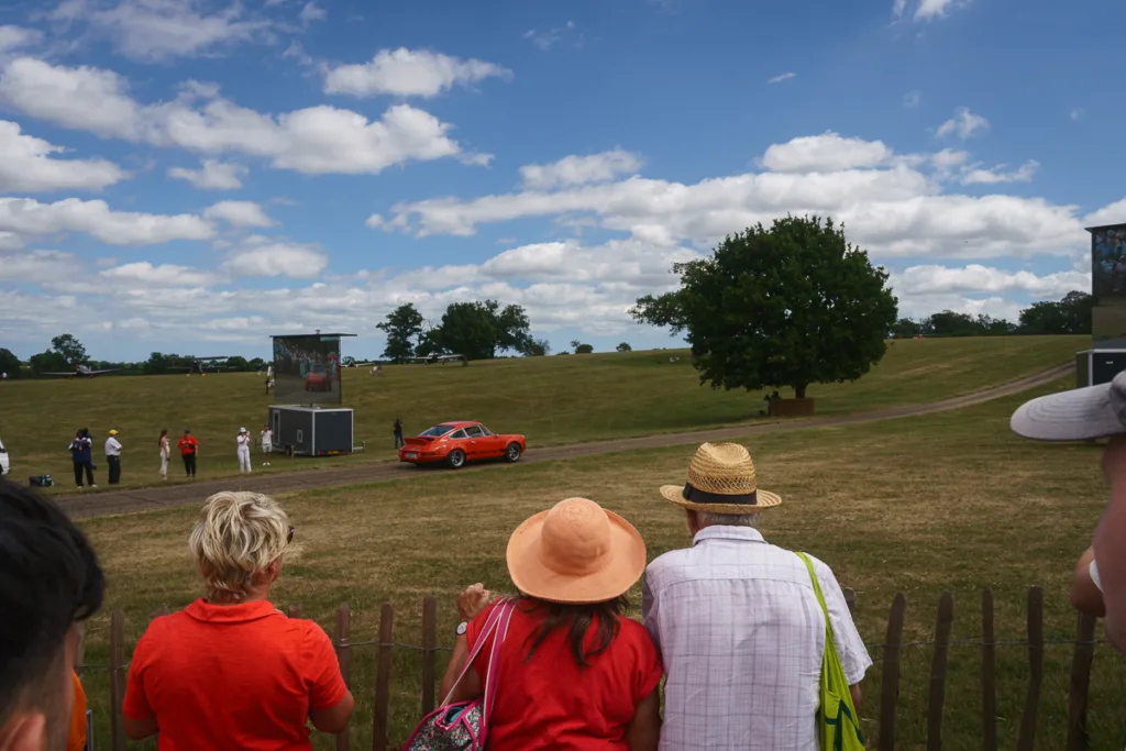 Spectators watching a red car on grassy field.