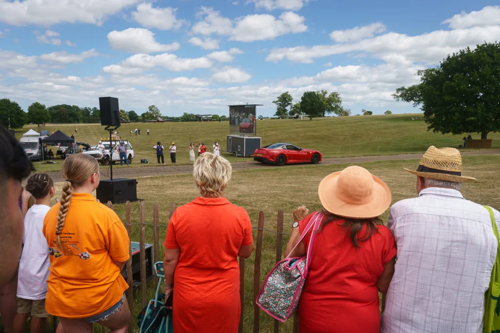 Spectators watching red sports car at outdoor event.