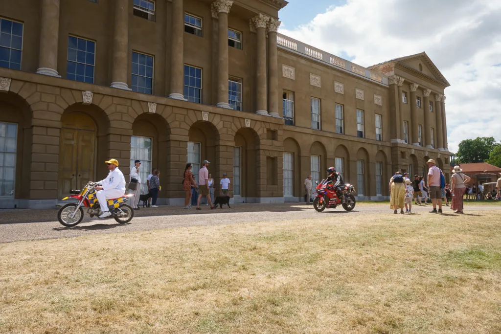 People and motorcycles outside stately home