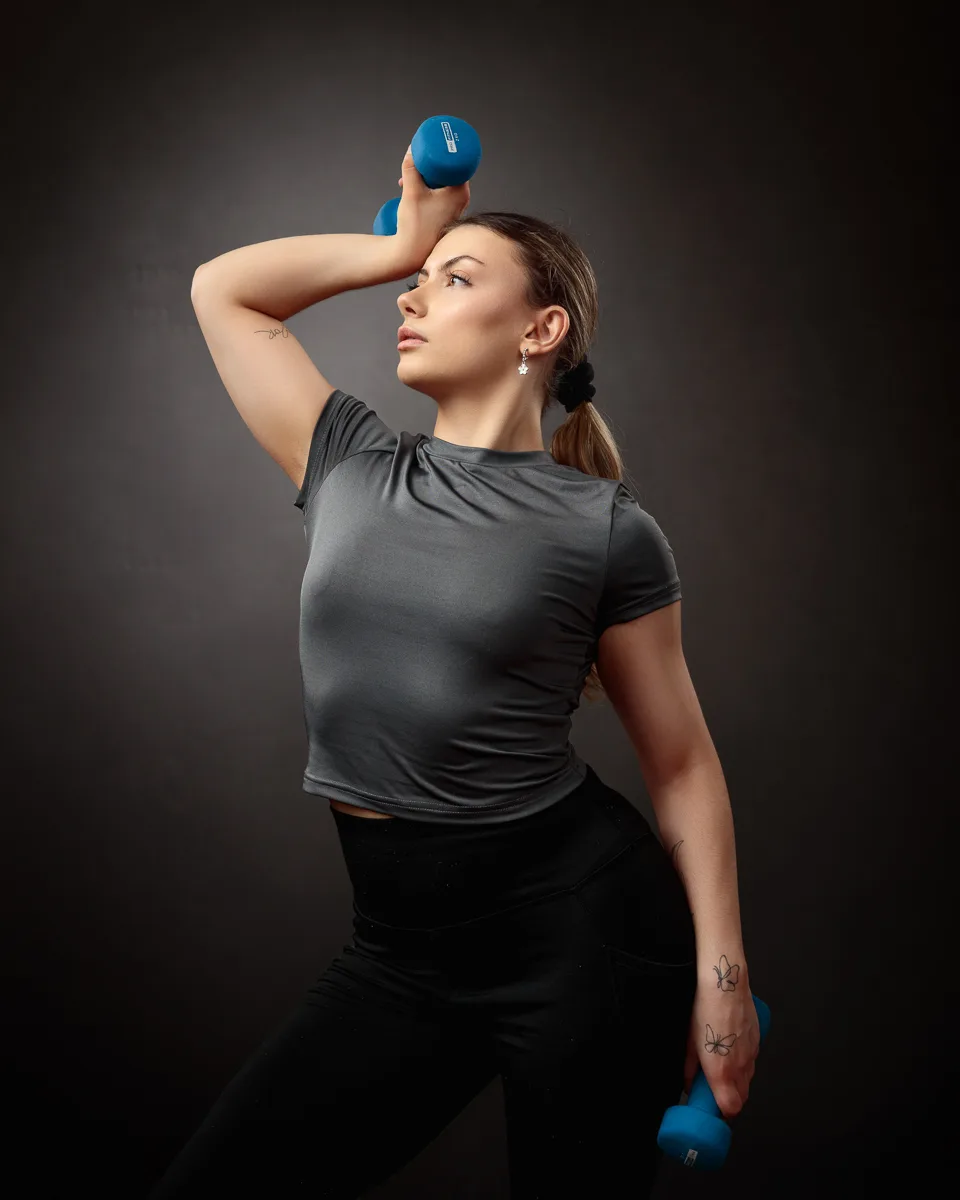 Woman exercising with blue dumbbells, grey outfit.