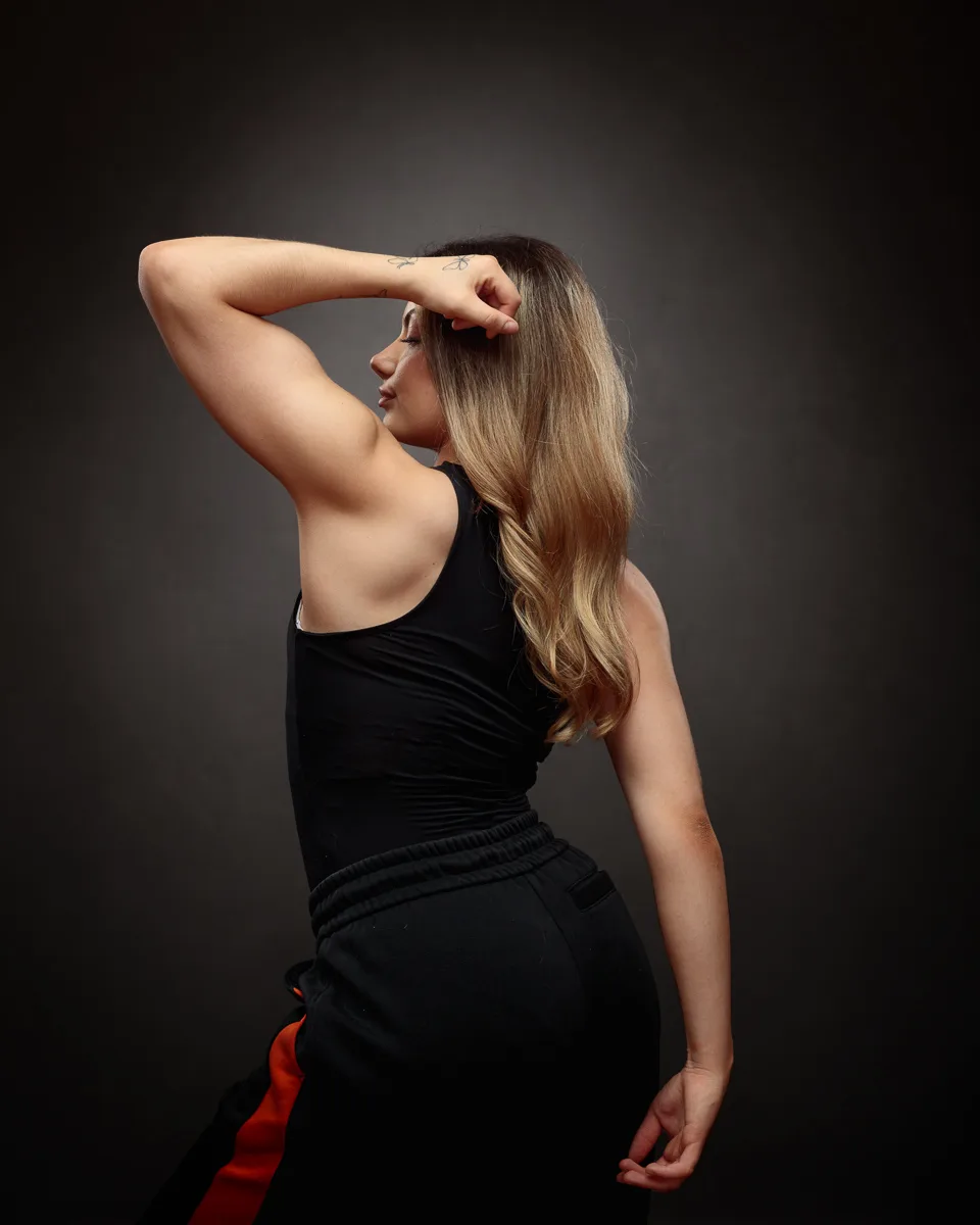 Woman flexing arm in athletic pose, side view.