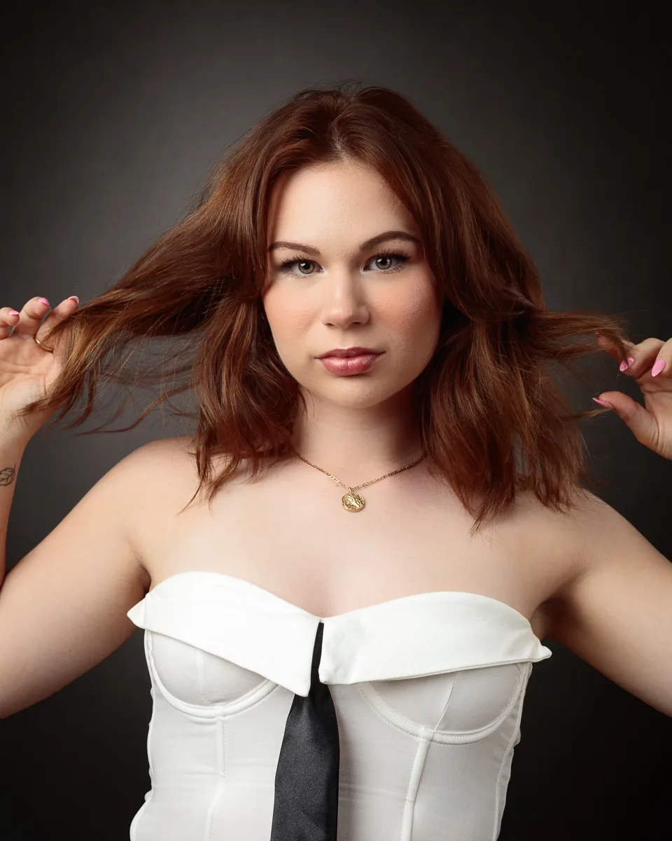 Woman posing in white strapless dress, holding hair