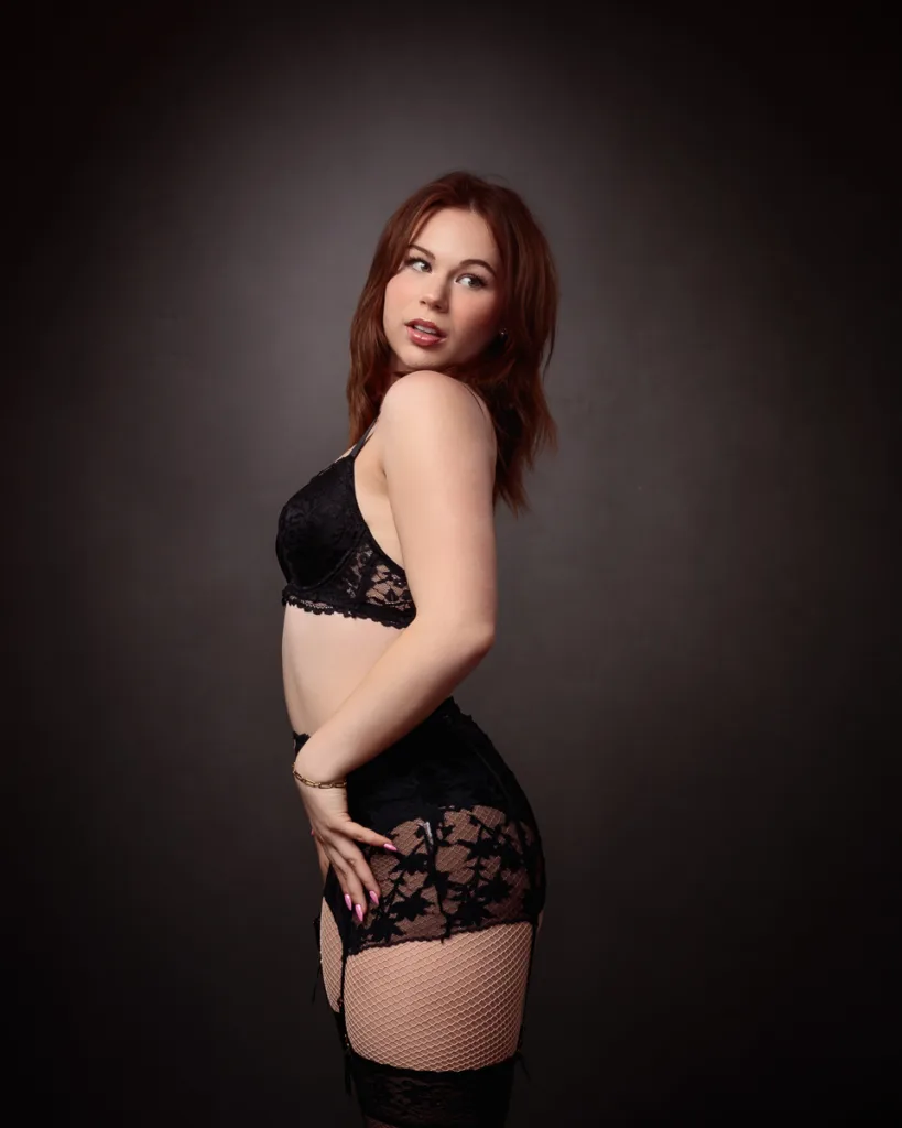 Woman posing in black lace lingerie against dark background.