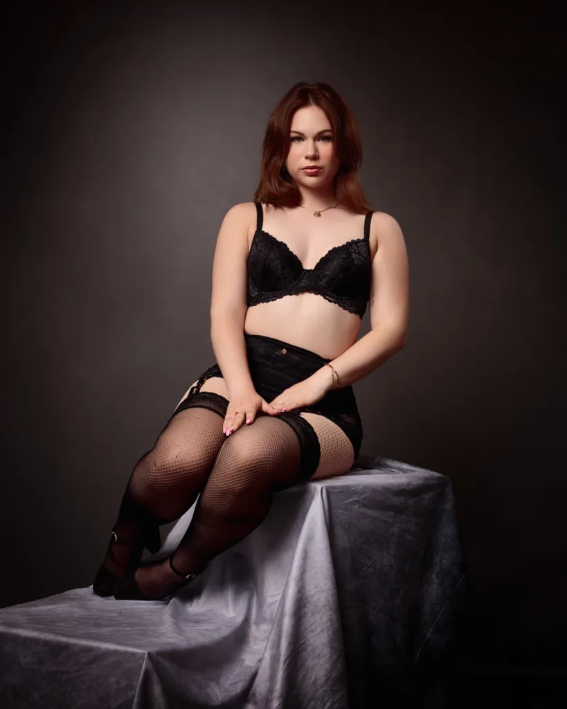 Woman in black lingerie on fabric-covered table.