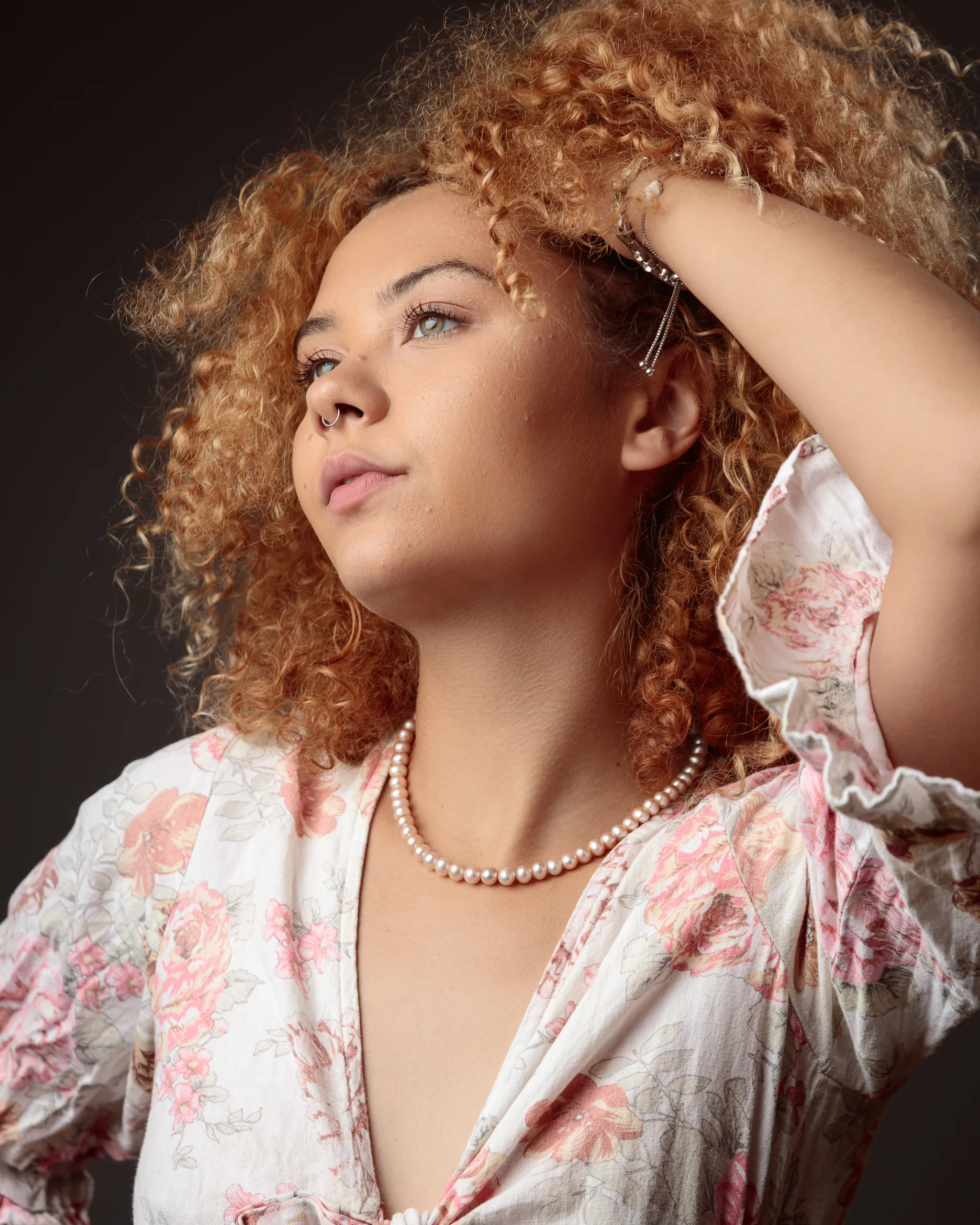 Woman with curly hair in floral dress, thoughtful expression.