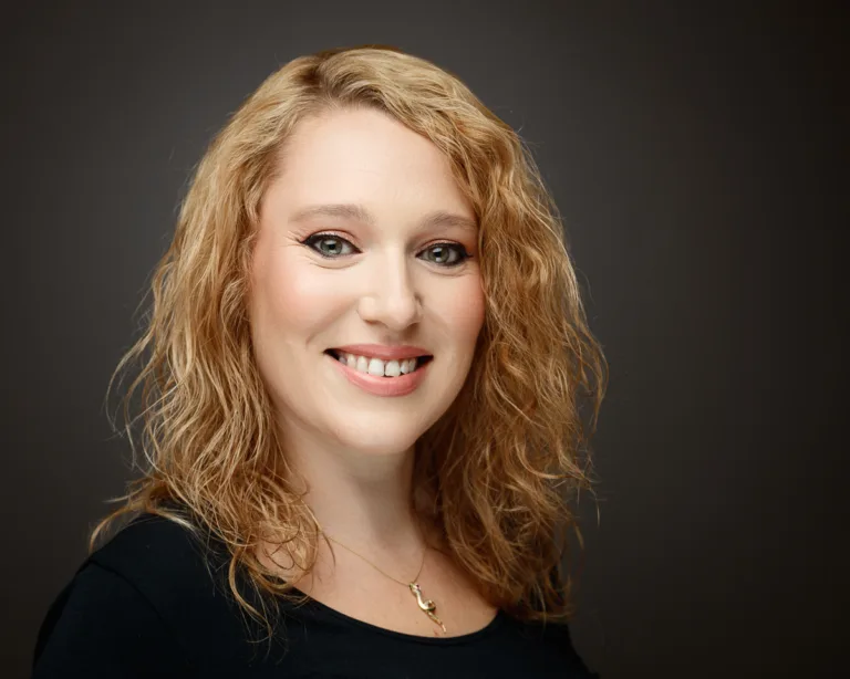 Smiling person with curly hair and necklace.