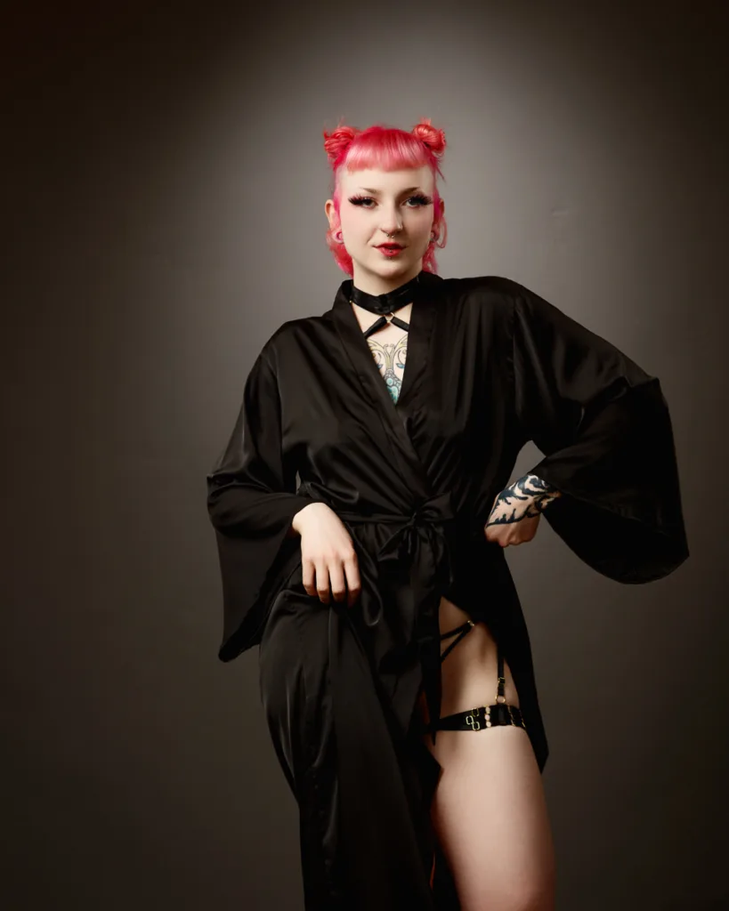 Person with pink hair in black robe posing.