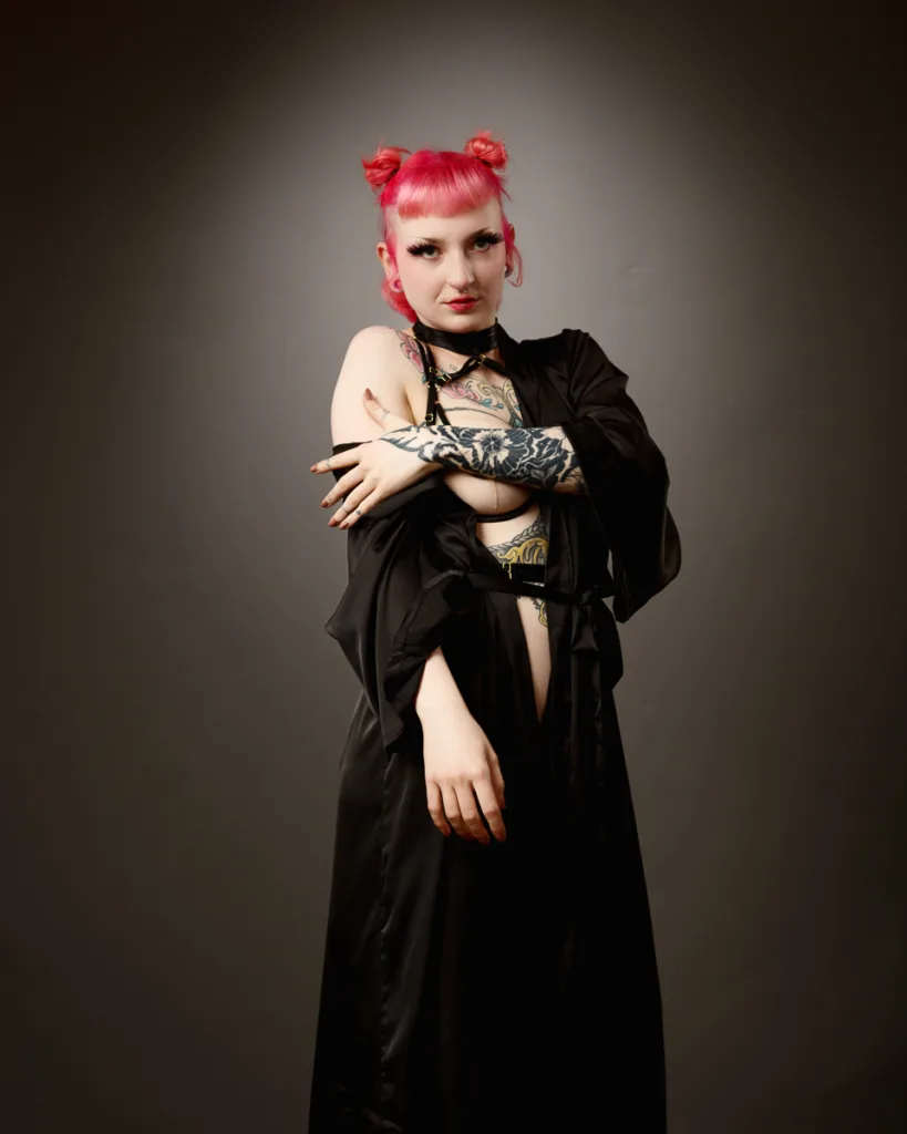 Person with tattoos and pink hair poses confidently.