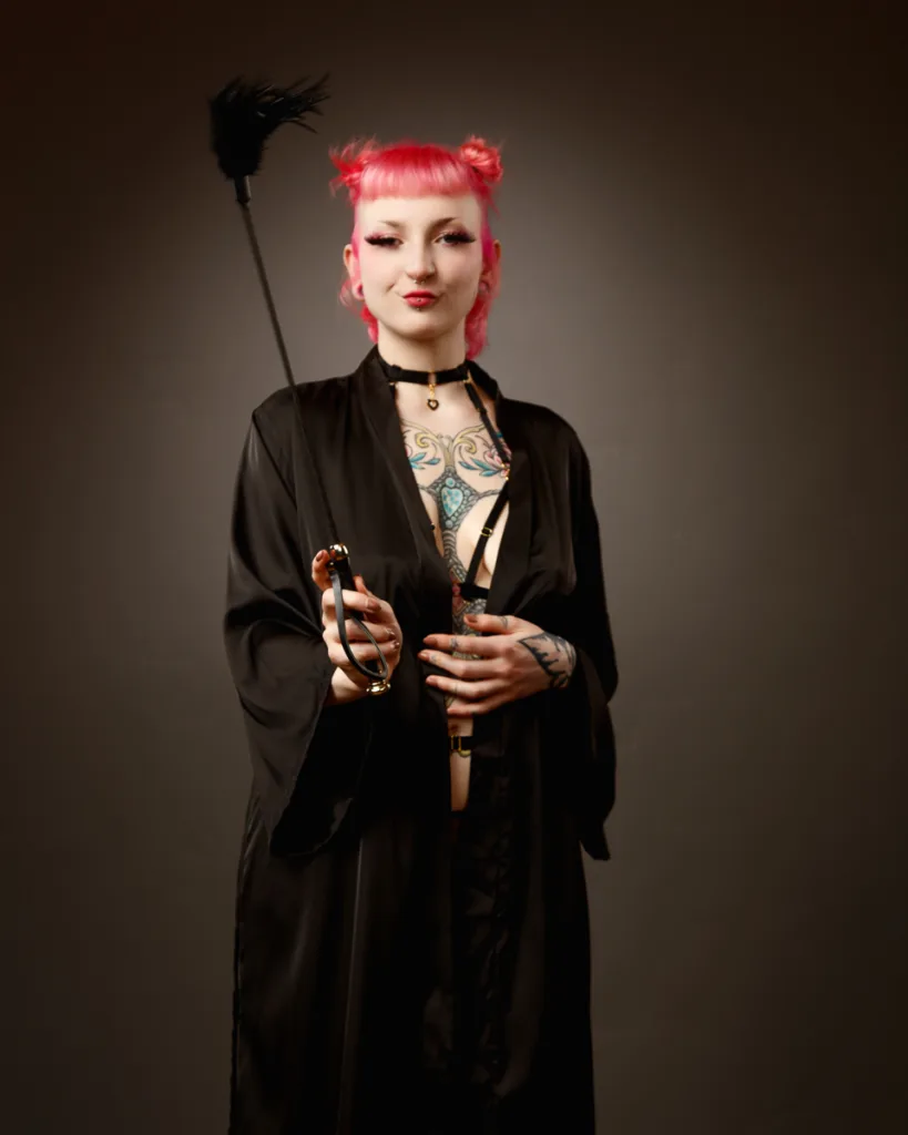 Person with pink hair and tattoos holding a toy.