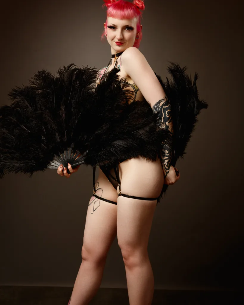 Person with pink hair holding black feather fans.