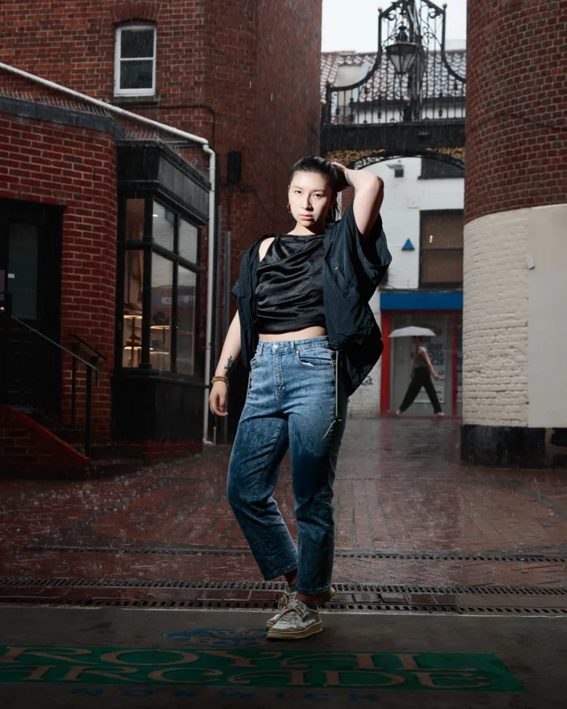 Person posing in rainy urban alley.