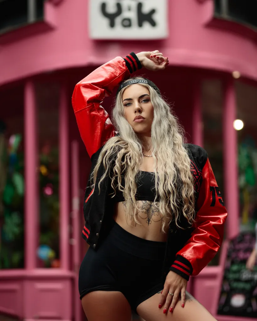 Woman posing in red jacket outside pink storefront.