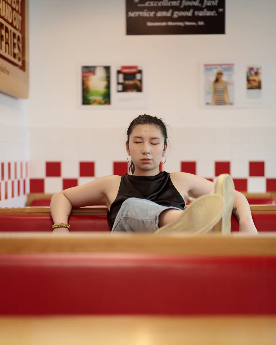 Person relaxing in a red diner booth, eyes closed.