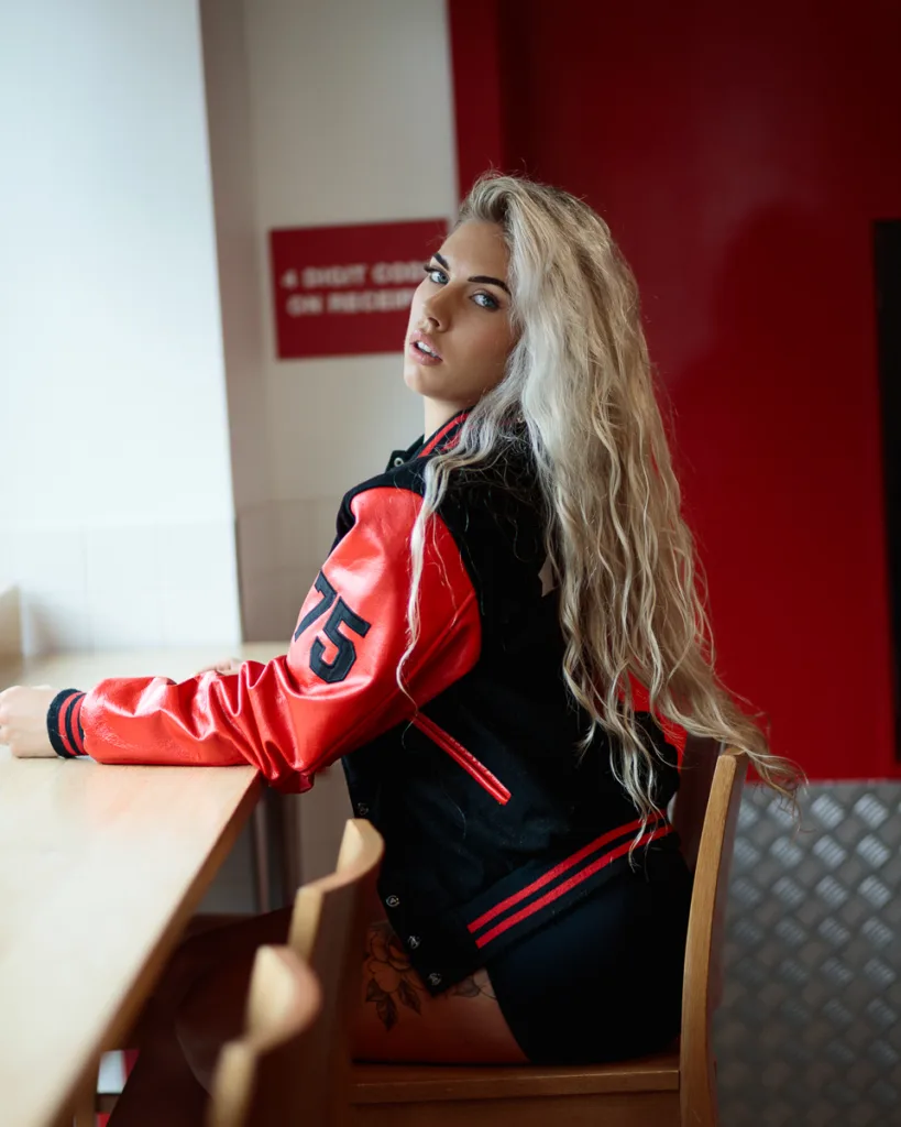 Person in varsity jacket sitting at wooden table.
