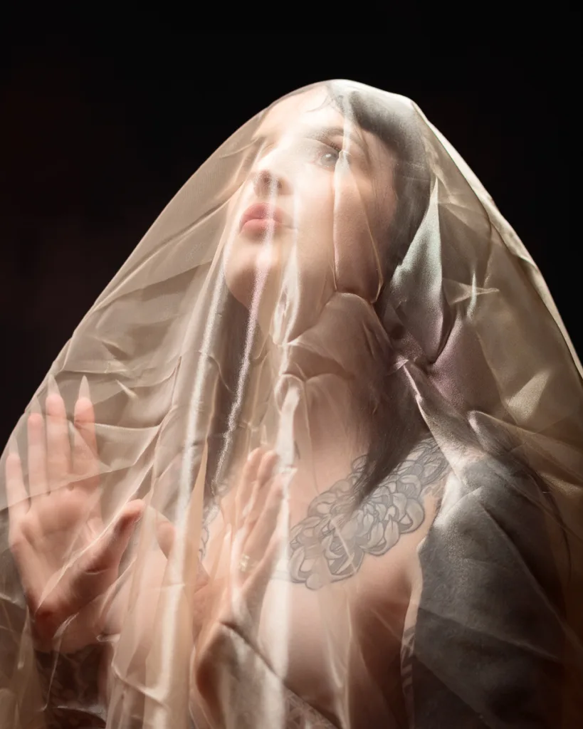 Woman under sheer fabric with tattoo, looking up.