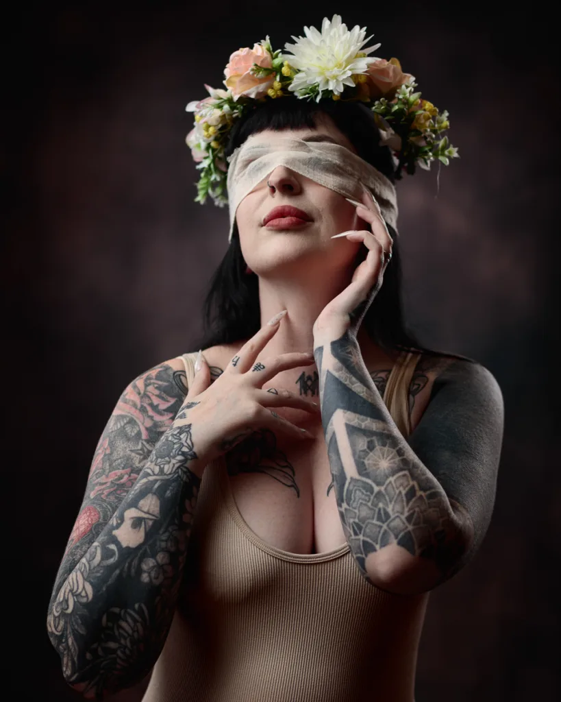 Tattooed woman with flower crown and bandaged eyes.