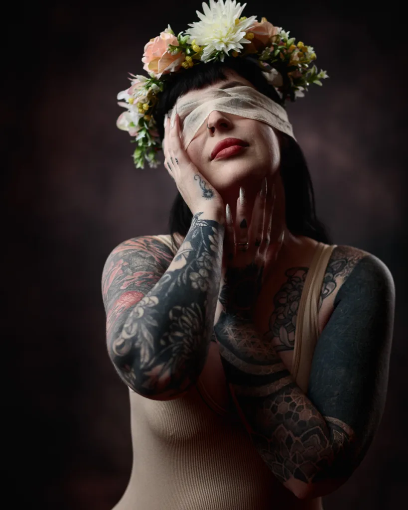 Tattooed person with floral crown, bandaged eyes.