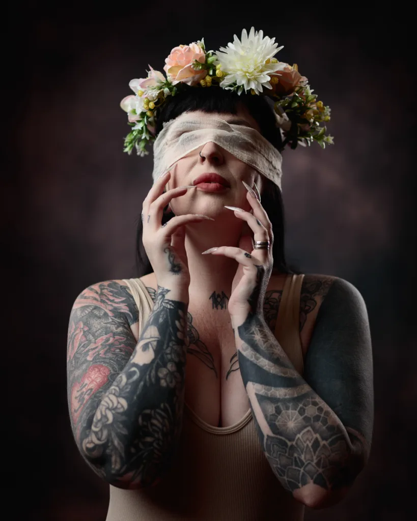 Tattooed woman with floral crown, eyes covered by bandage.