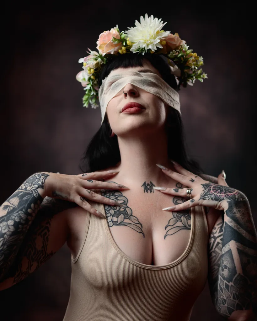 Tattooed woman with floral crown, blindfolded.