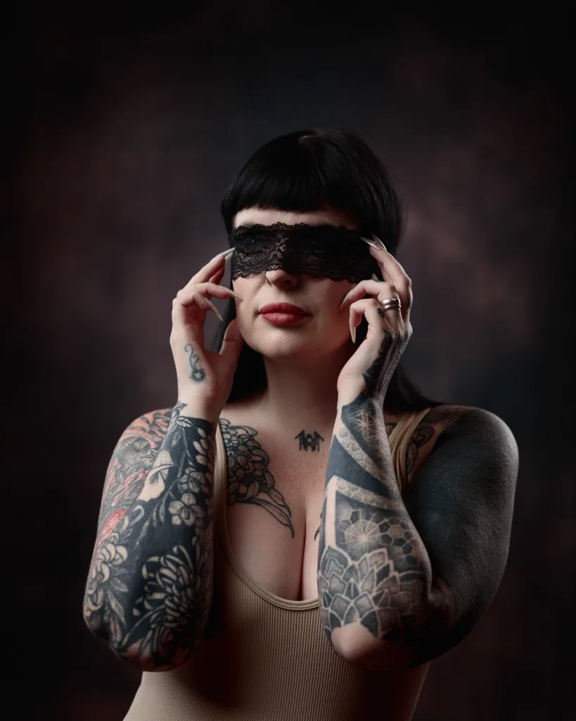 Tattooed woman wearing lace blindfold, artistic portrait