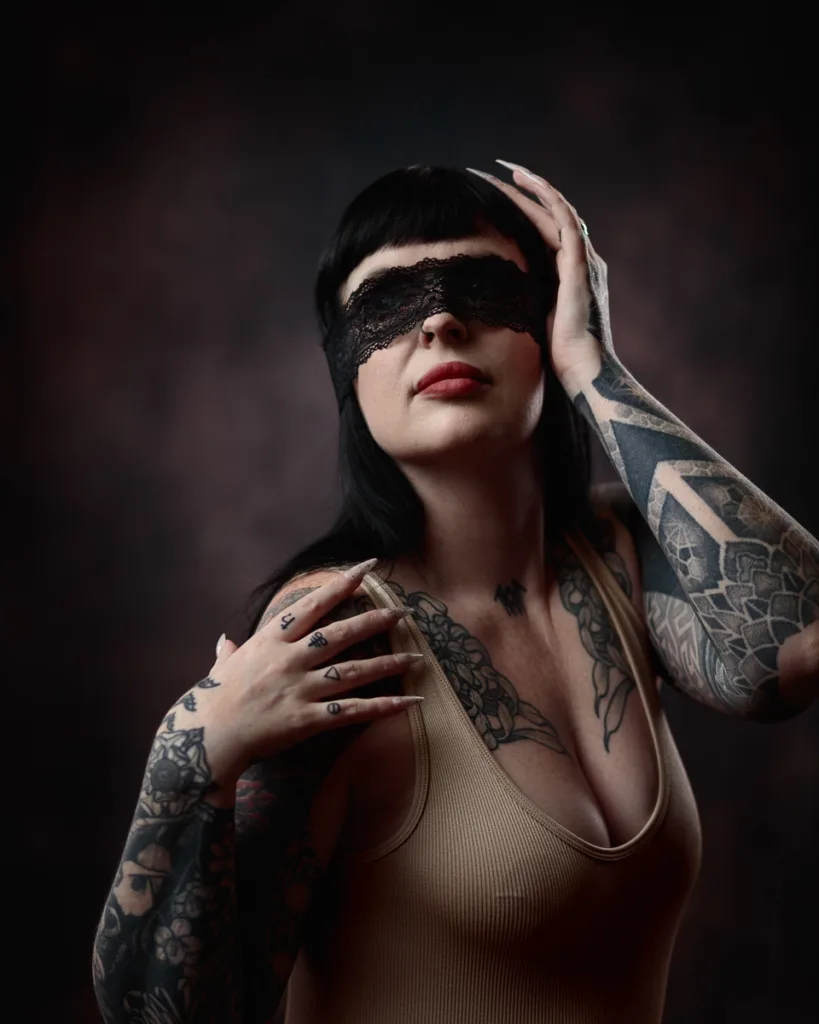 Tattooed woman wearing lace blindfold and beige top.