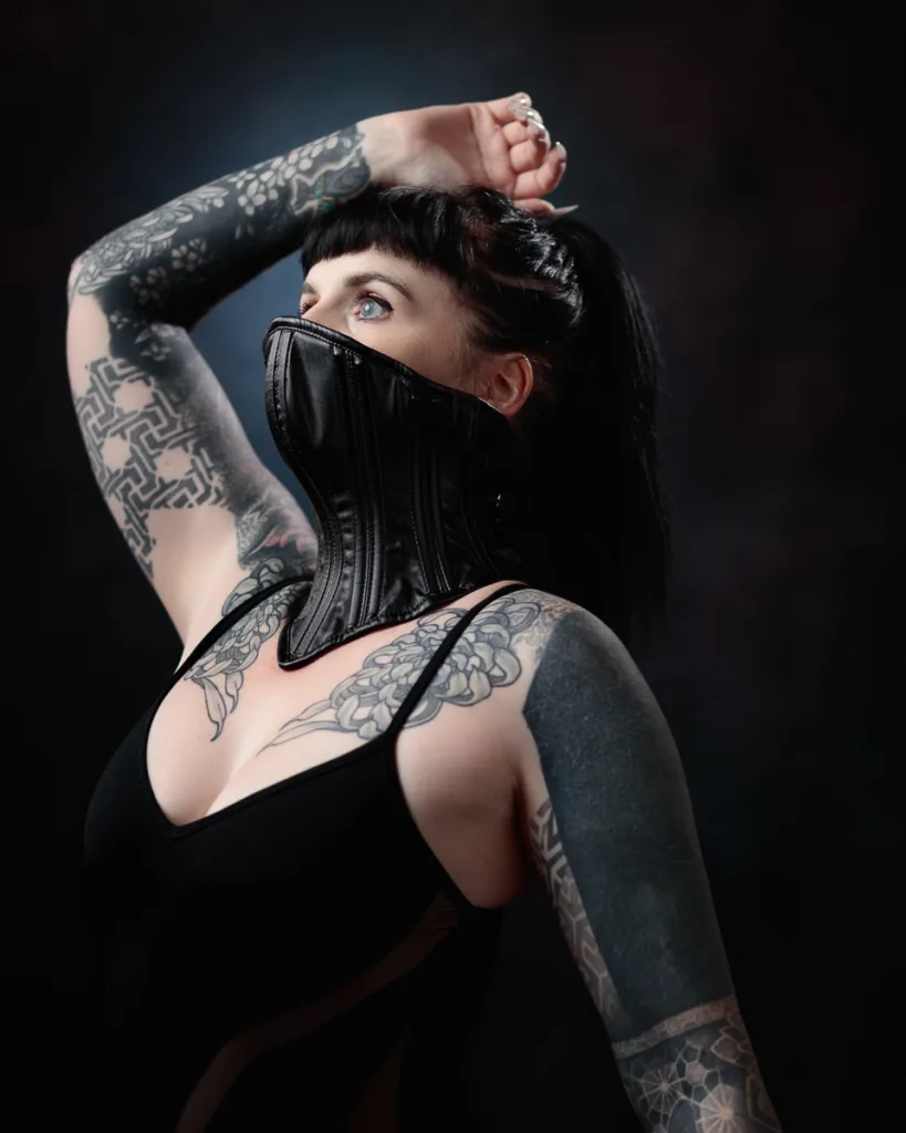 Tattooed model in black corset posing confidently.