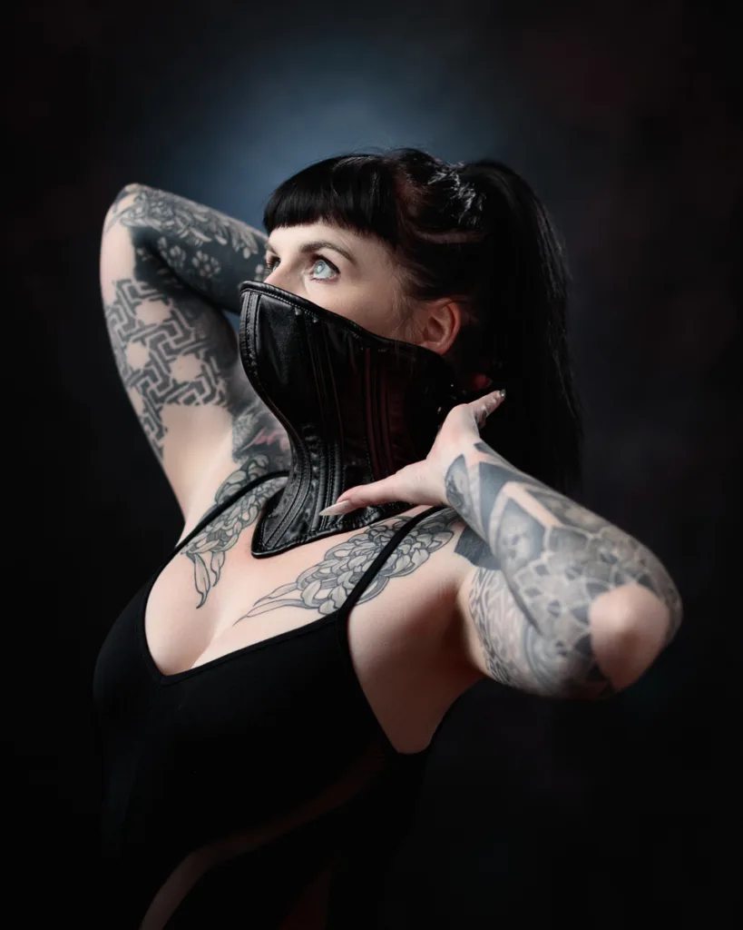 Tattooed woman wearing black bodysuit, stylish corset.