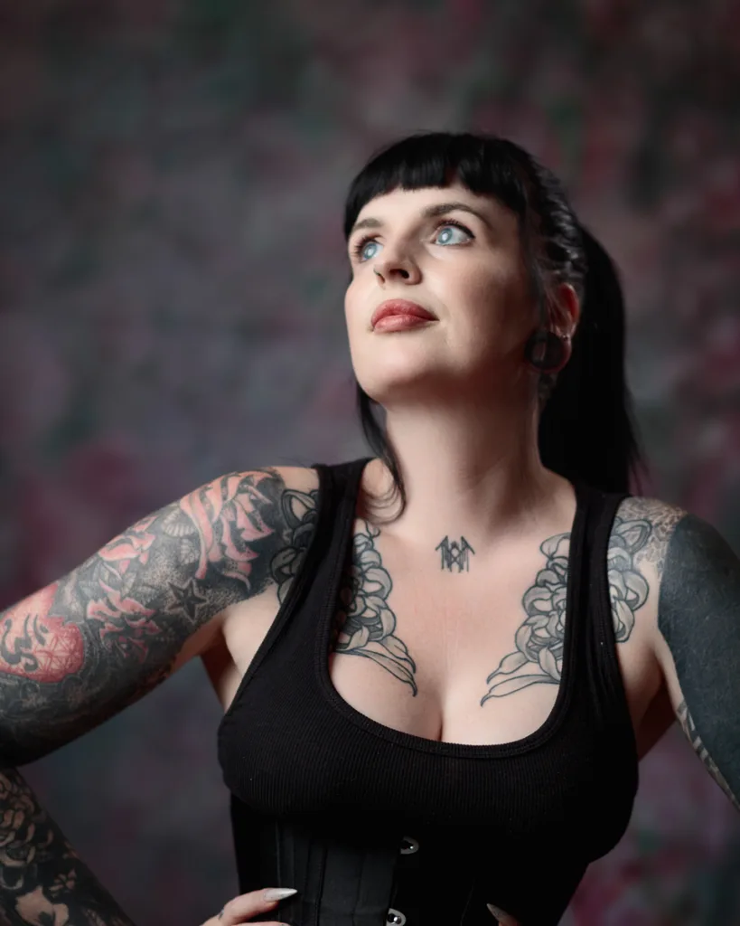 Woman with tattoos looking upwards, wearing black top.