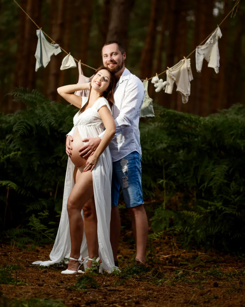 Pregnant couple in forest with baby clothes line.