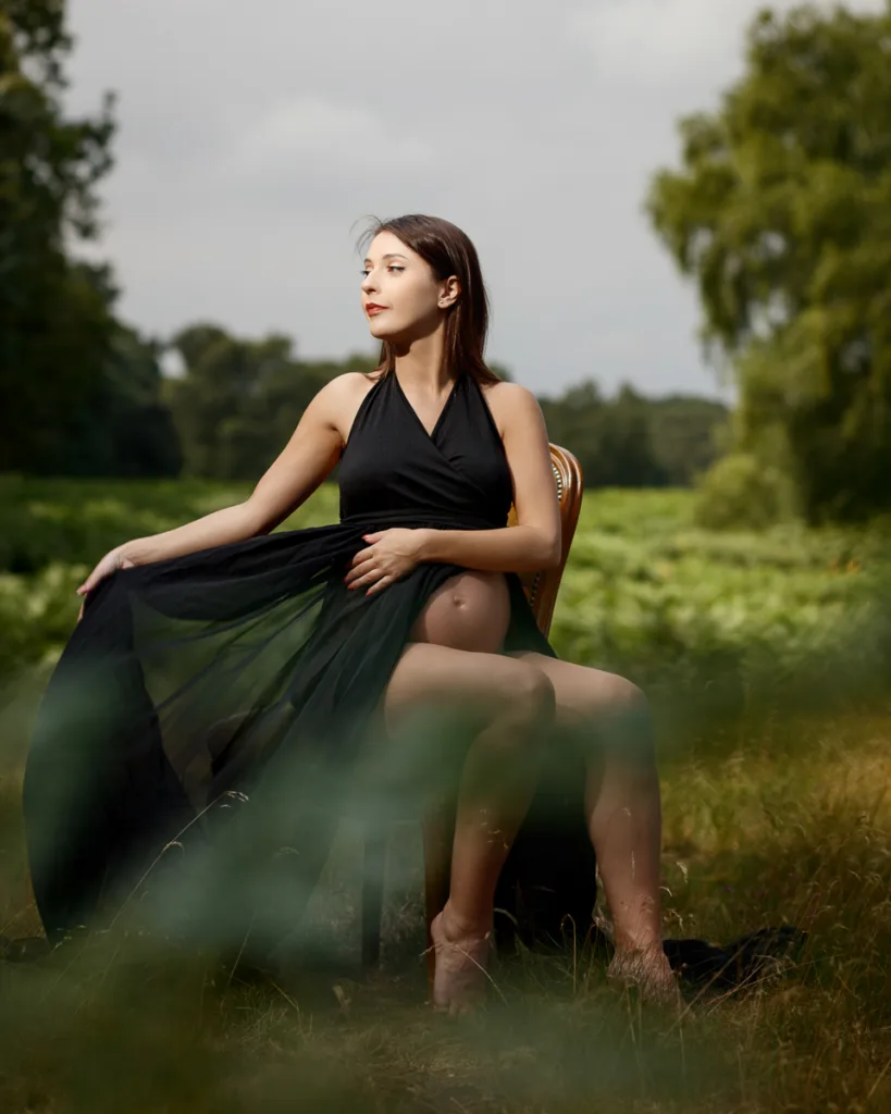 Pregnant woman in black dress sitting outdoors.