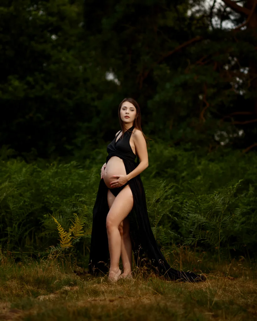 Pregnant woman in black gown standing outdoors.