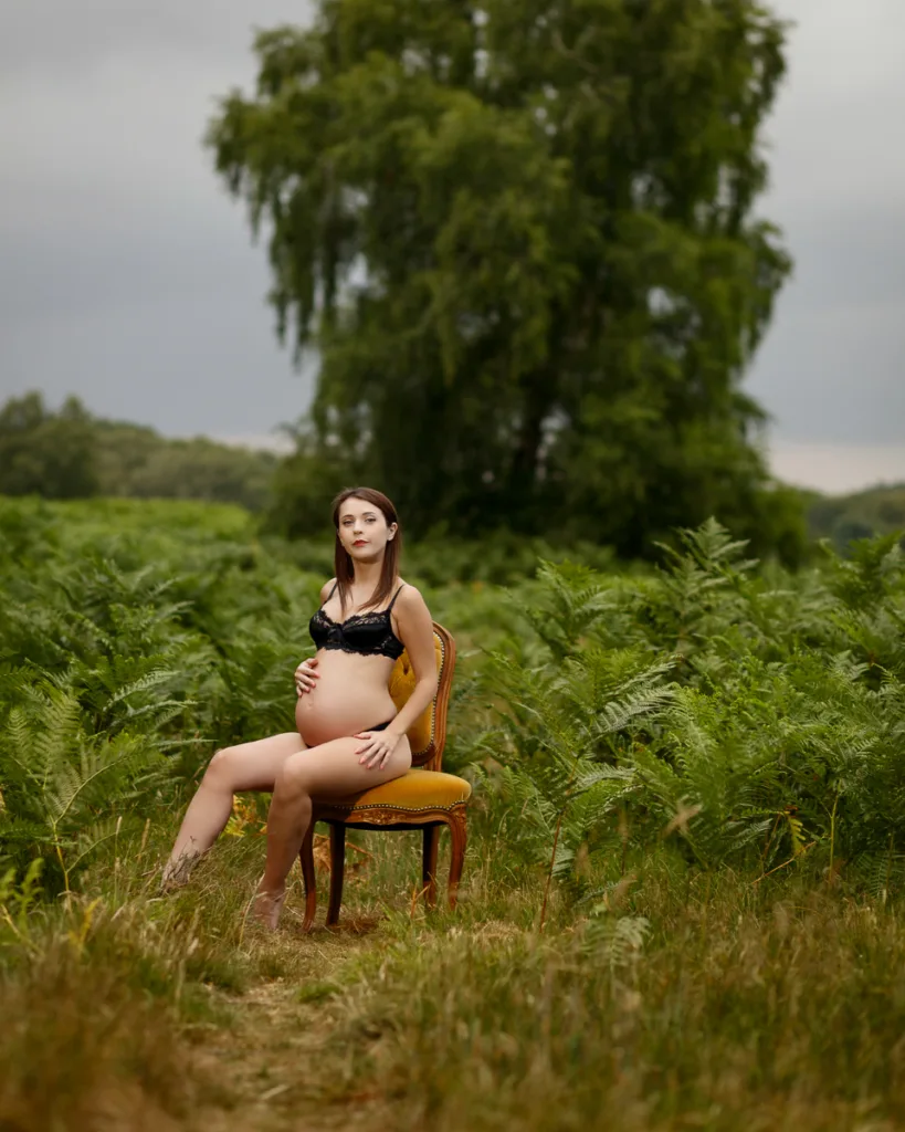 Pregnant woman sitting on chair in green field.