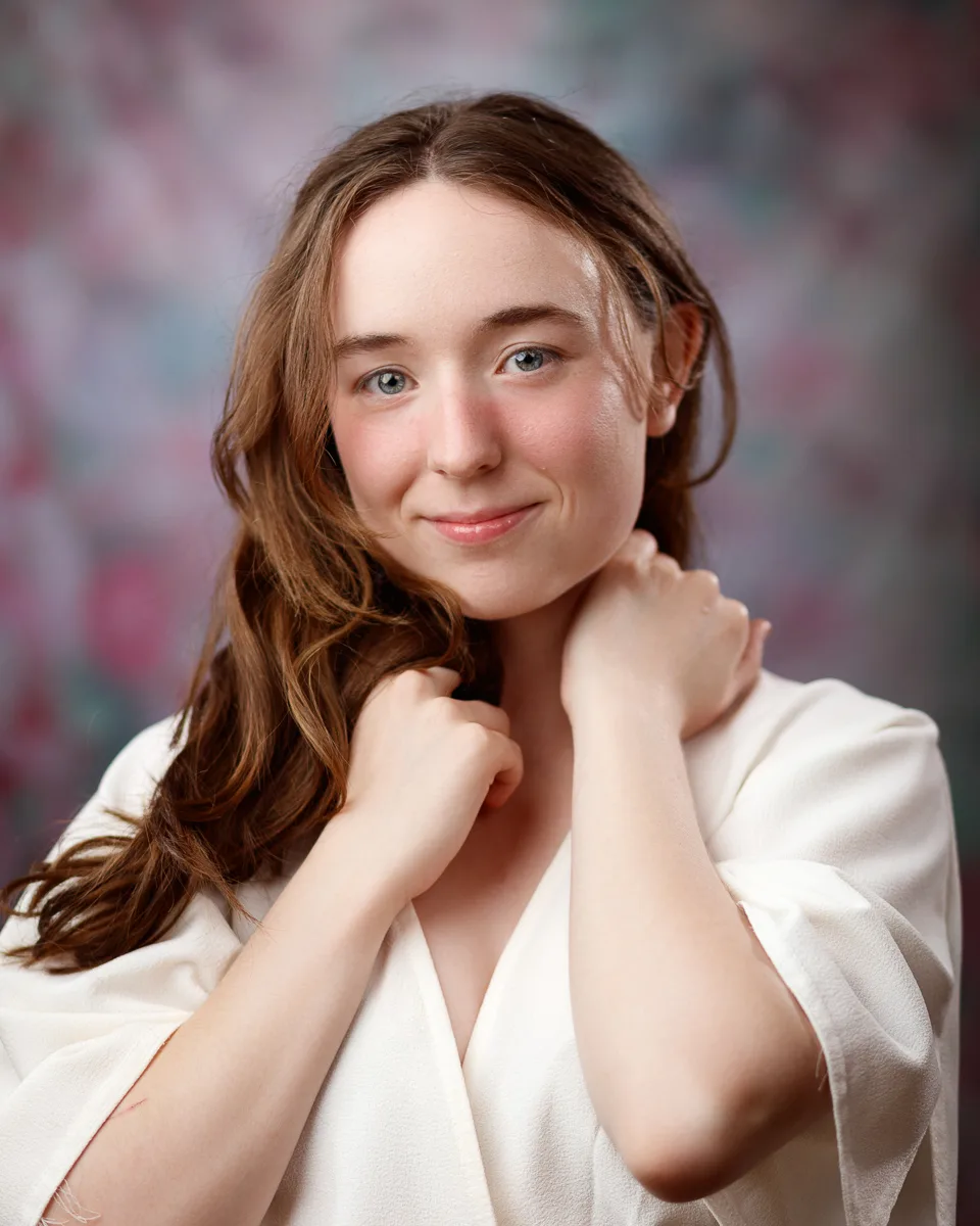 Smiling woman in white robe, colourful background.