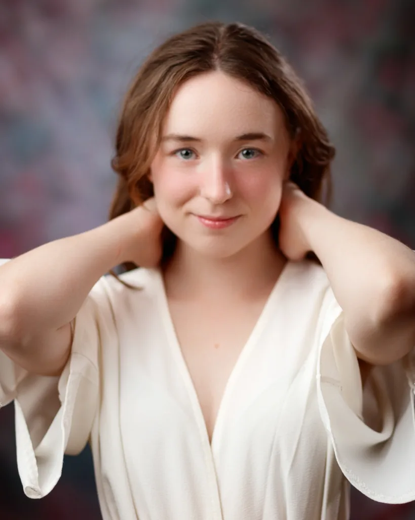 Person in white top, hands behind neck, smiling gently.