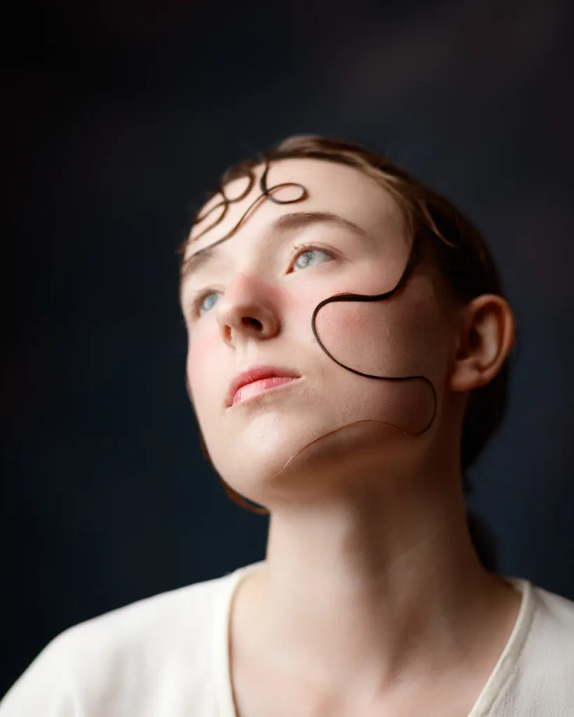 Person gazing upwards, hair styled artistically around face.